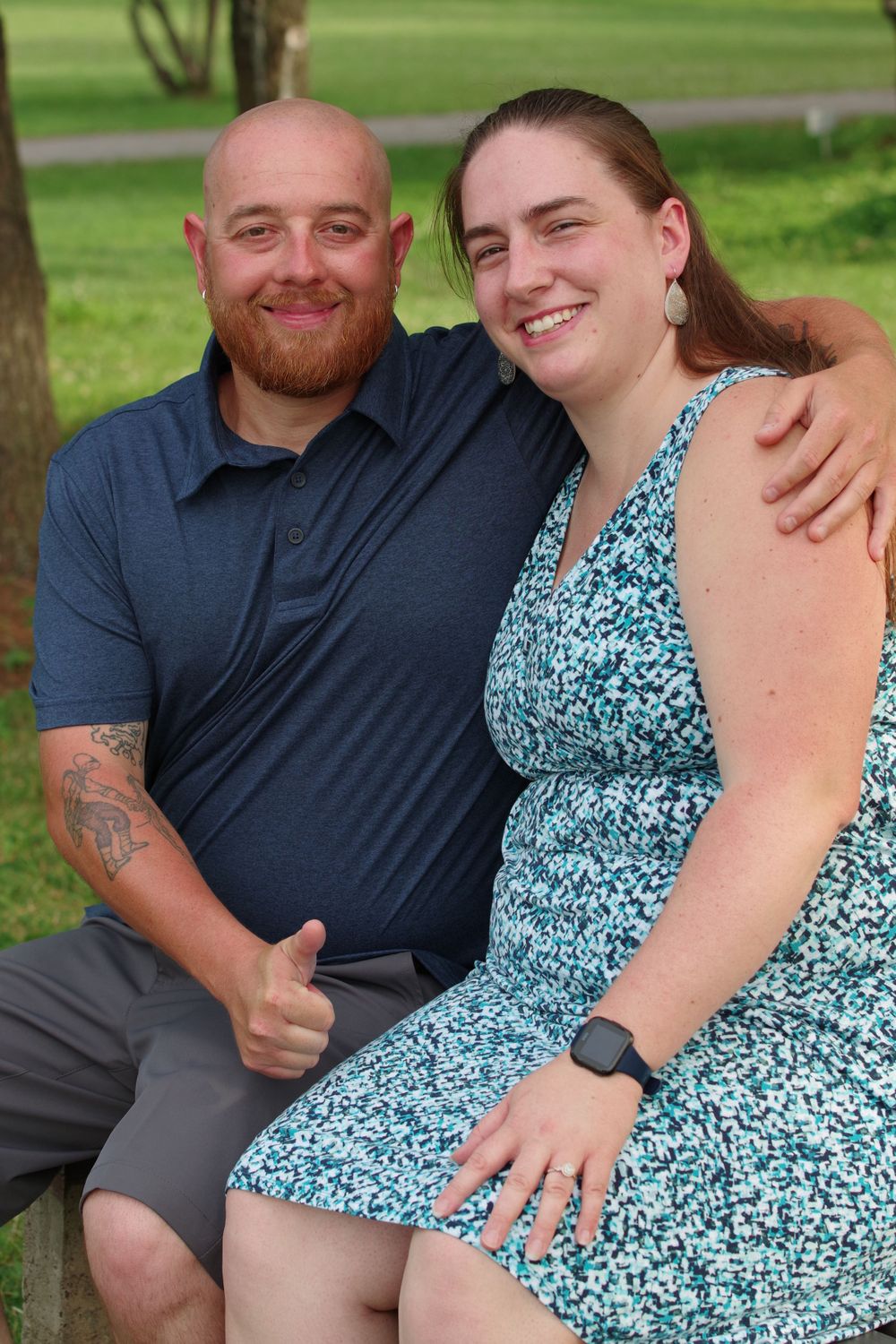 A couple sits together on a bench in a park setting on a sunny day.