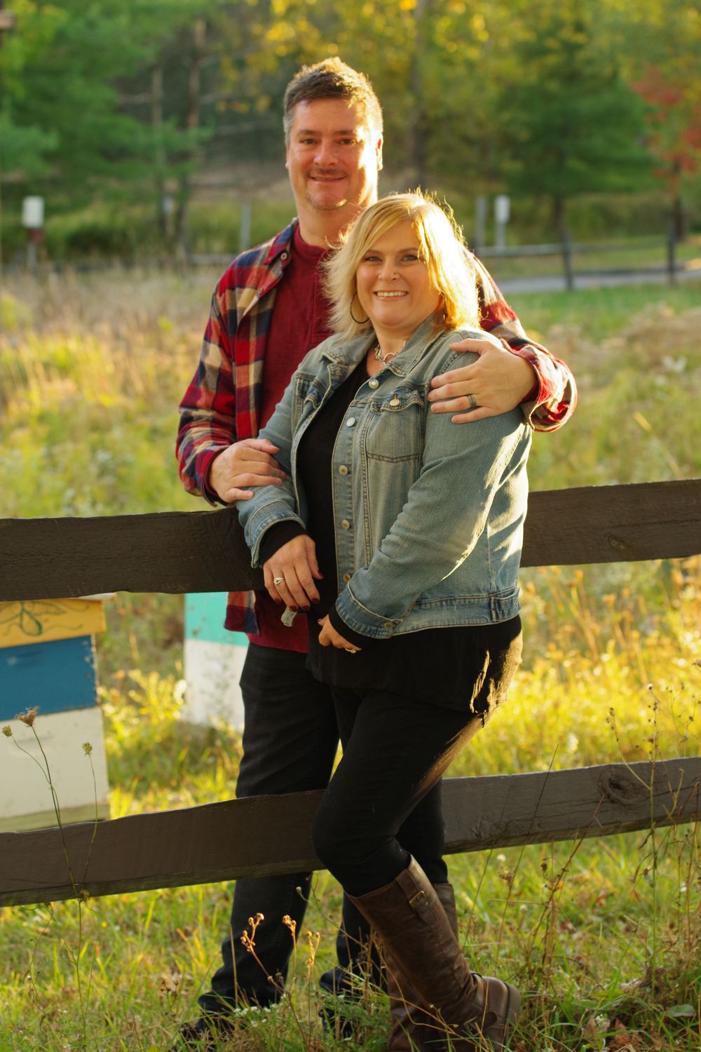 A couple leans against a wooden fence during golden hour in autumn.