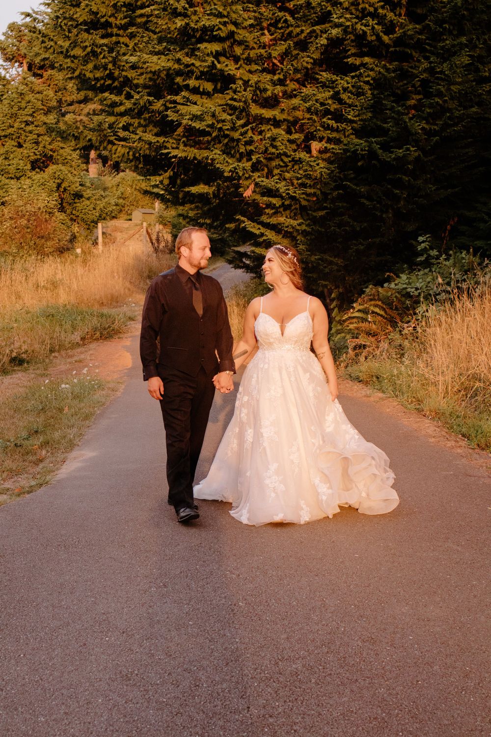 Bride and groom walking hand in hand down a sunlit path in golden hour light.