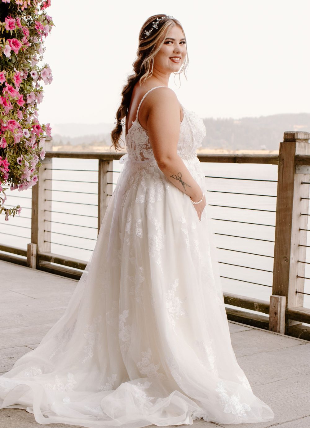 Bride in elegant lace A-line wedding gown smiling over shoulder on outdoor venue deck.