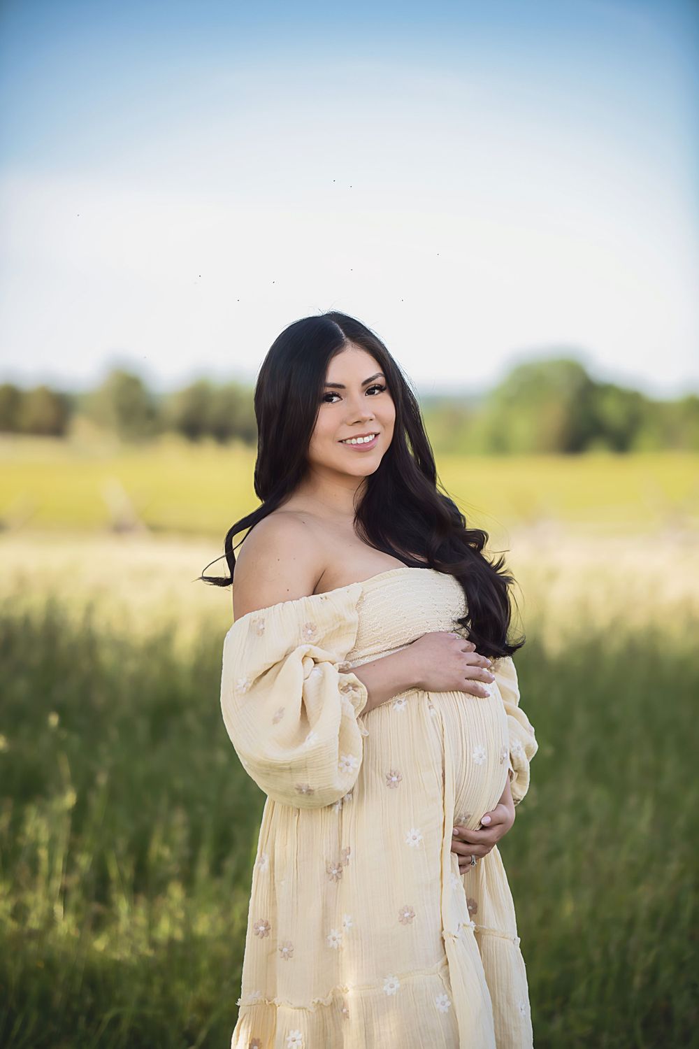 Maternity photos in cream dress against sunny field backdrop.