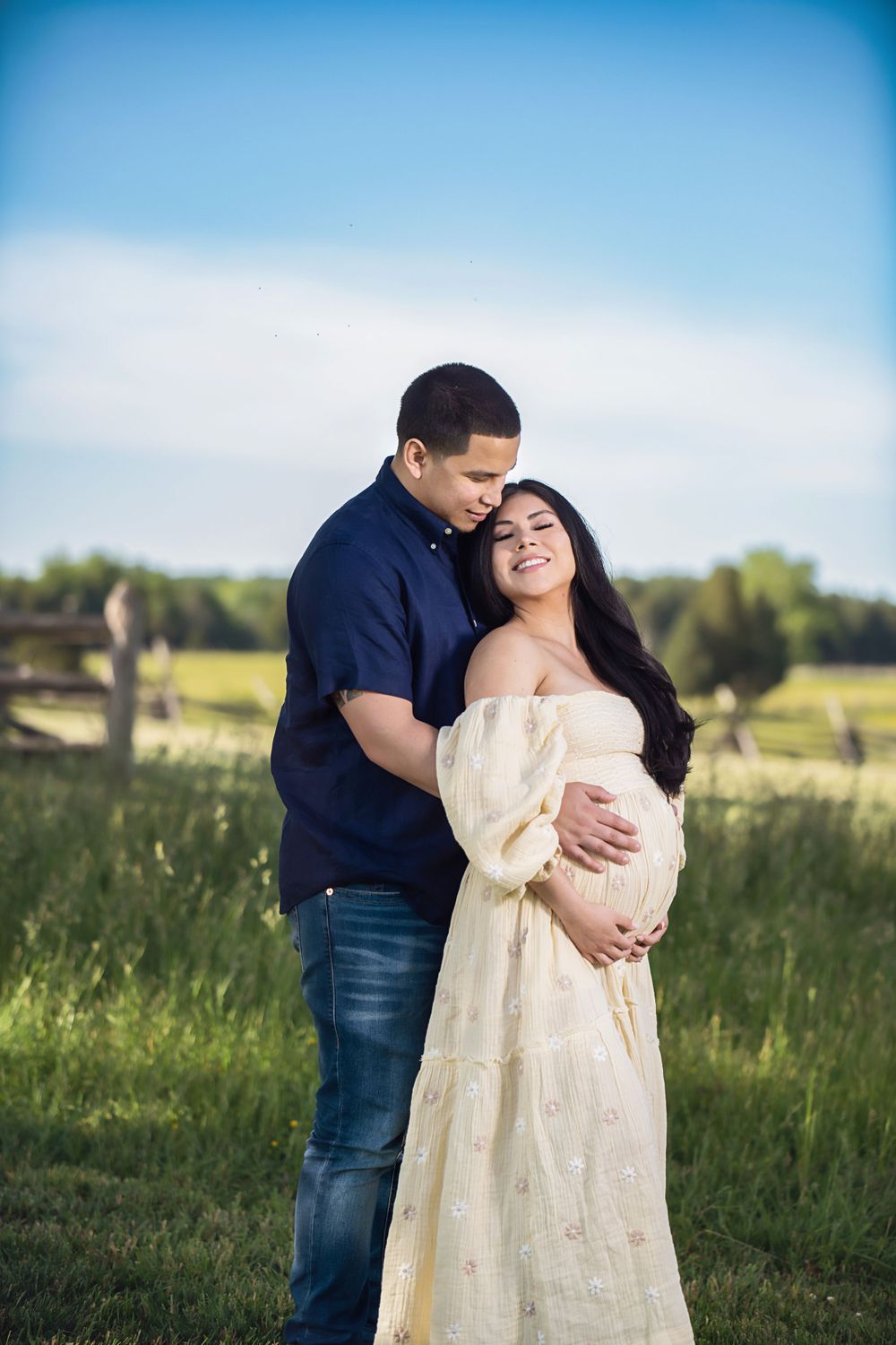 Couple embracing during outdoor maternity photoshoot in grassy field.