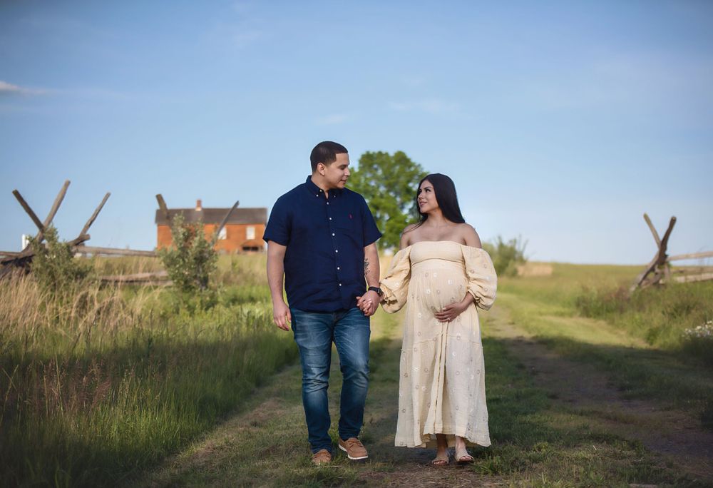 A romantic outdoor photoshoot in a rustic field with wooden fences and natural surroundings at sunset.