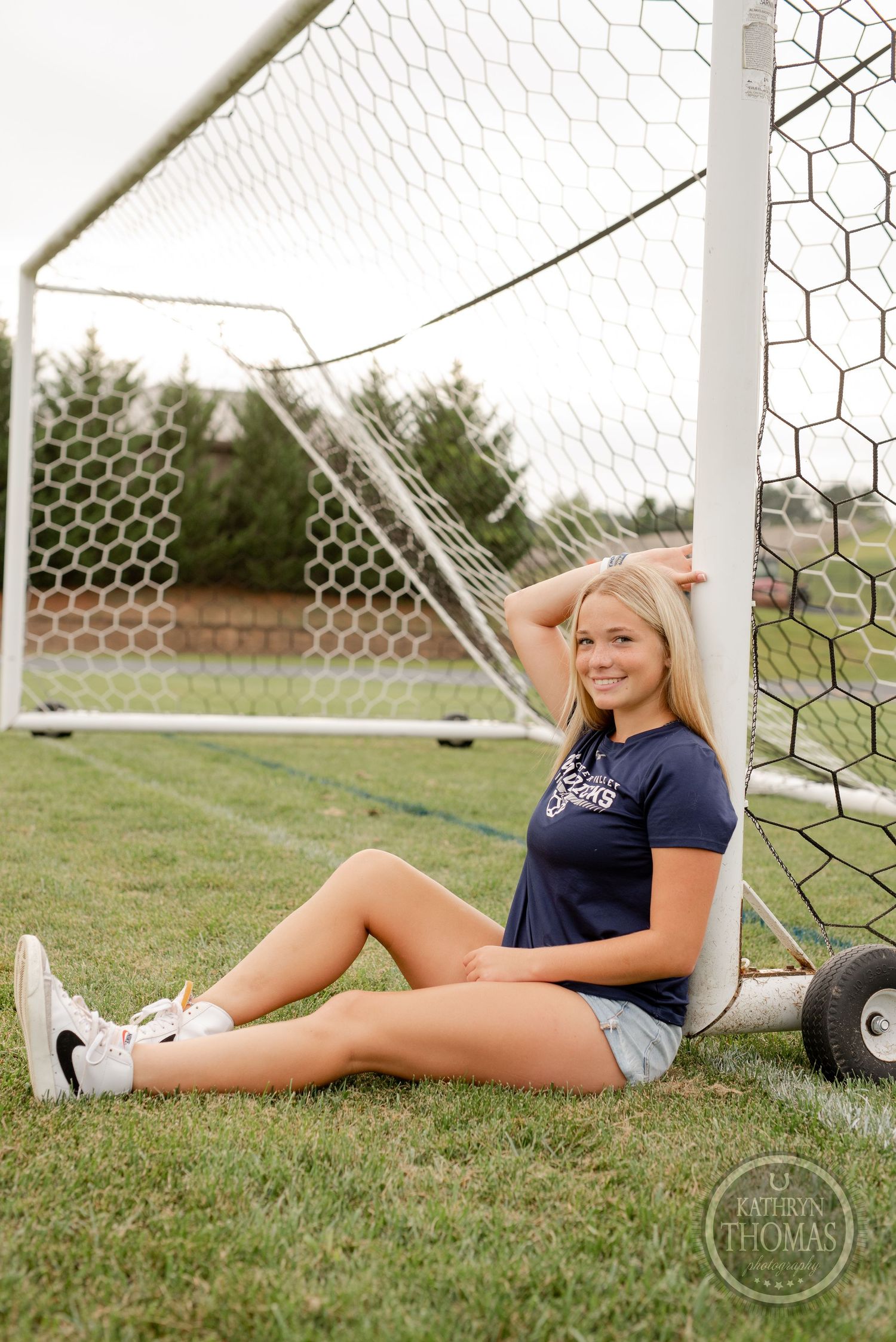 Athlete resting against soccer goal post on grass field.