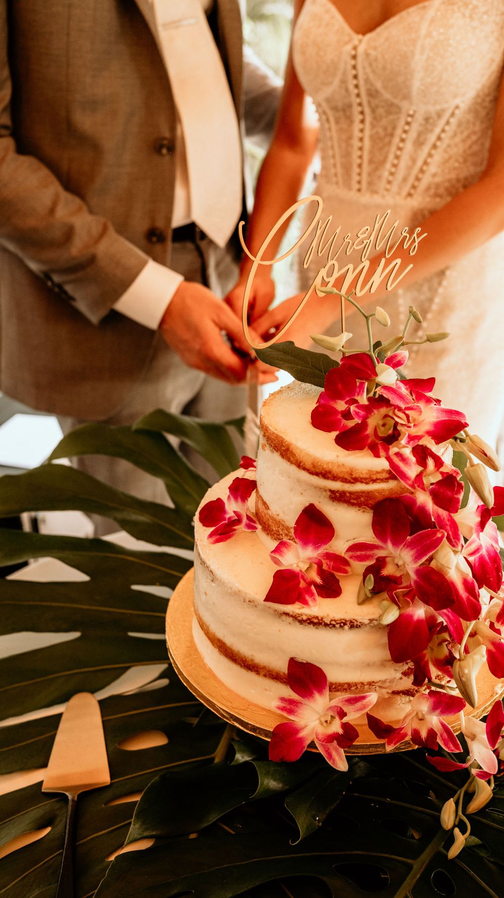 Wedding cake decorated with cascading red orchids and monstera leaves.