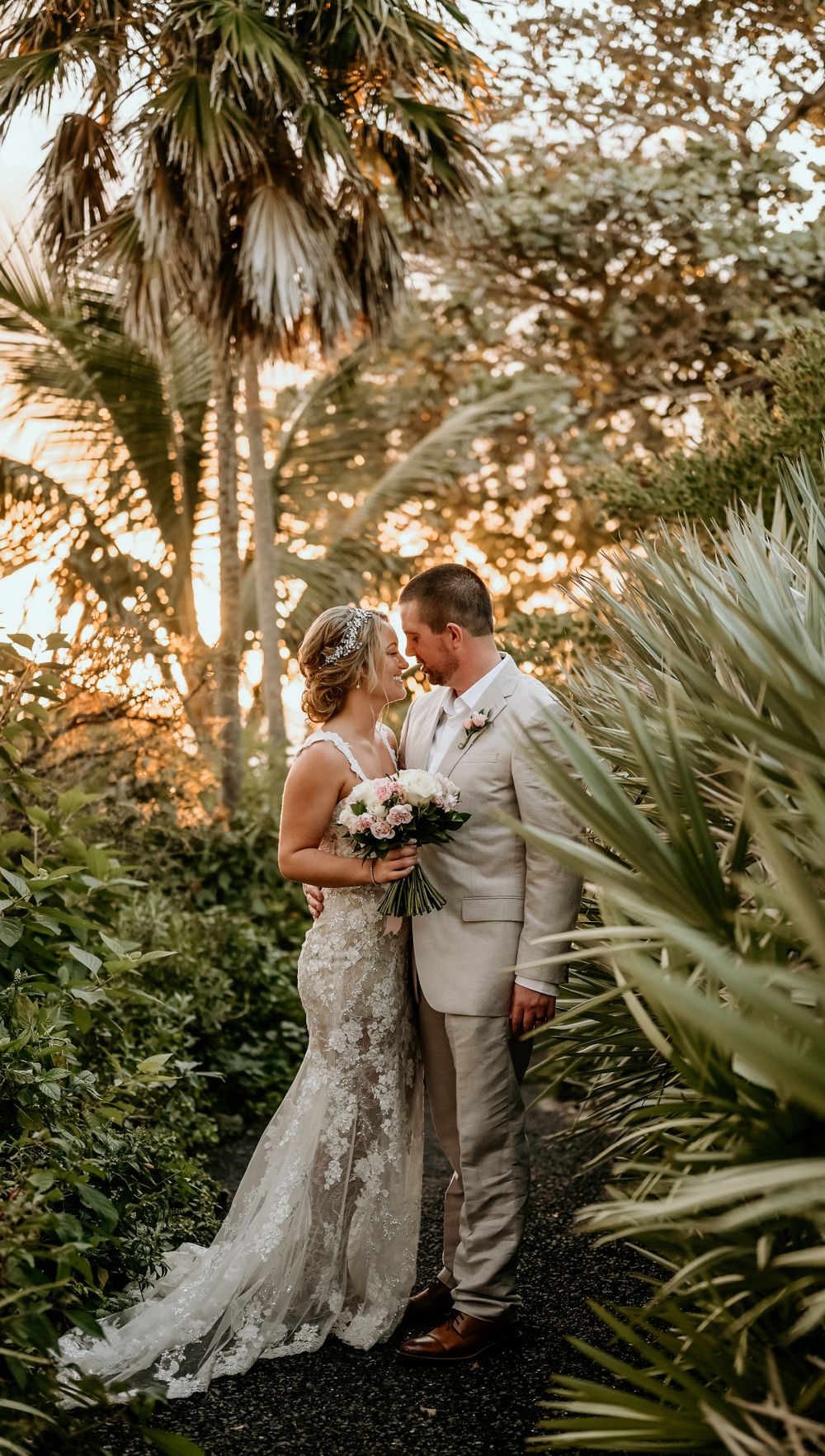 Tropical garden wedding portrait with palm trees and lace gown at sunset.