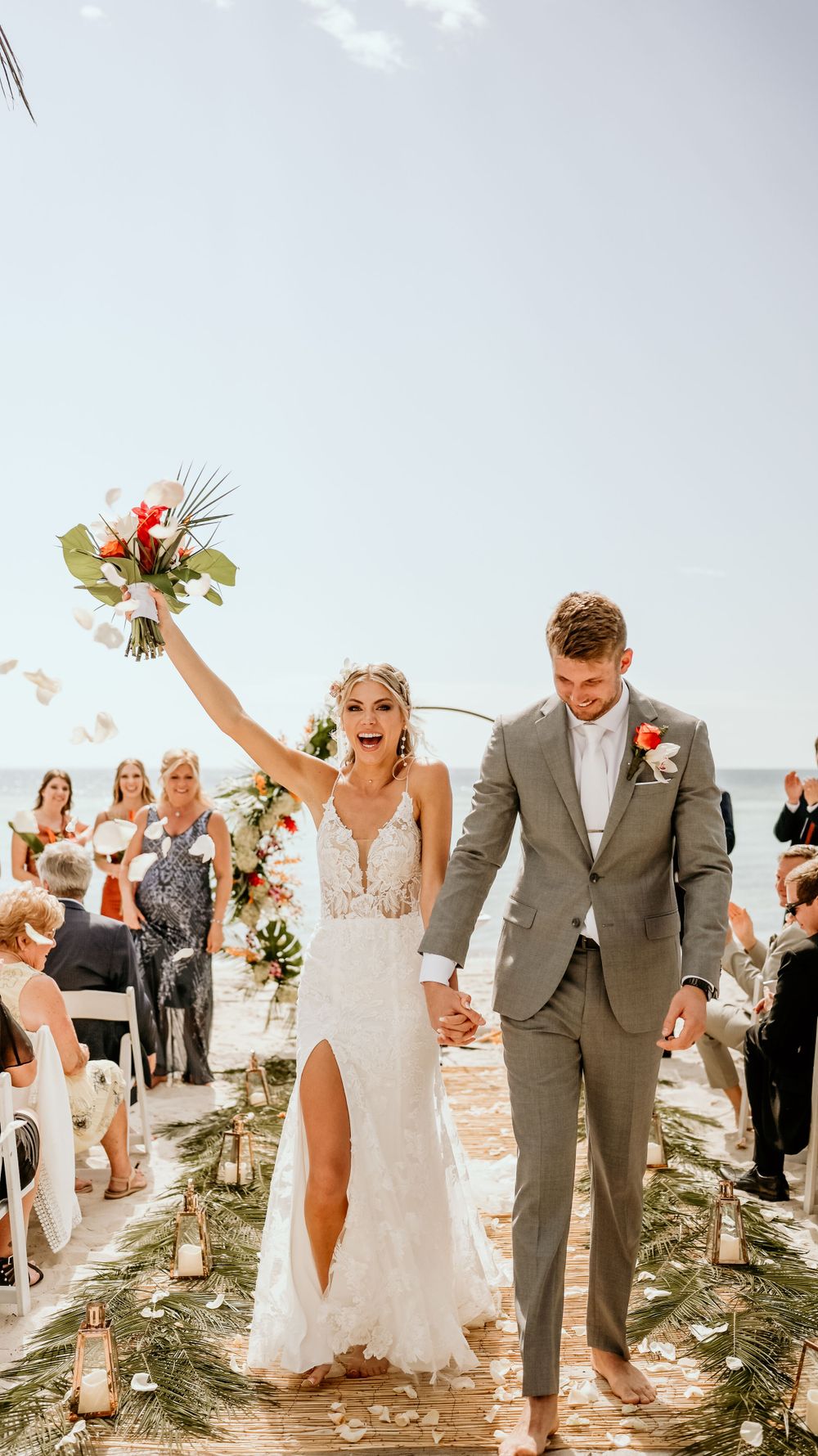 Newlyweds celebrating while walking down aisle decorated with tropical flowers.
