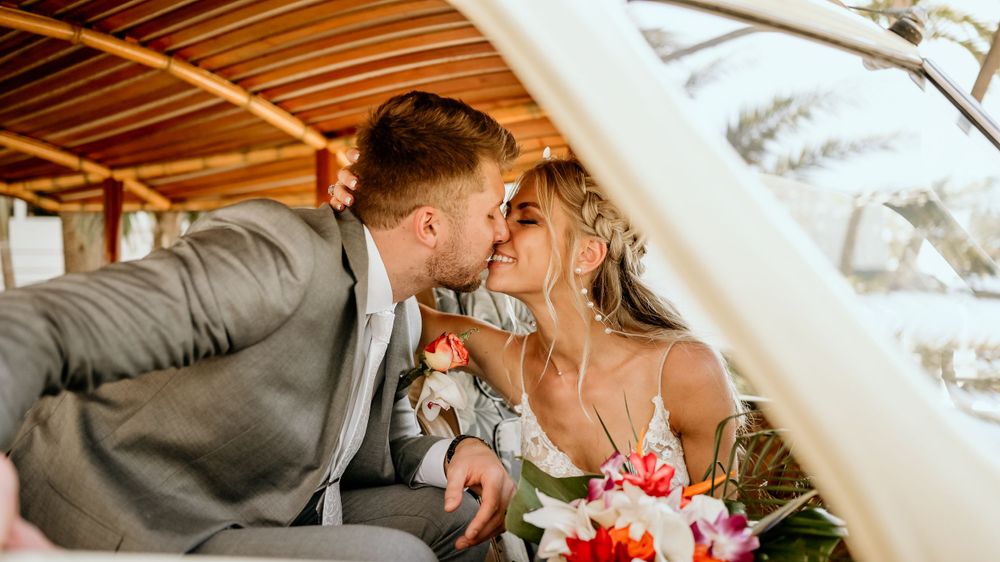Wedding couple sharing a tender moment under a wooden canopy with bridal bouquet.