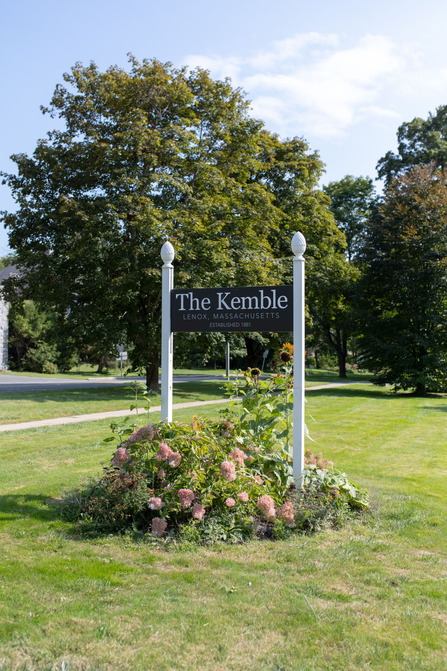 The Kemble venue sign surrounded by landscaped flower garden and green trees.