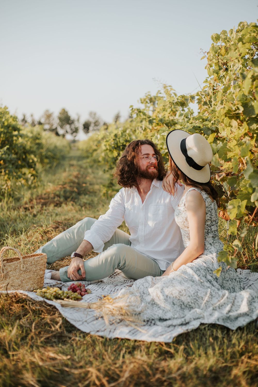 A couple enjoys a picnic among vineyard rows on a blanket.