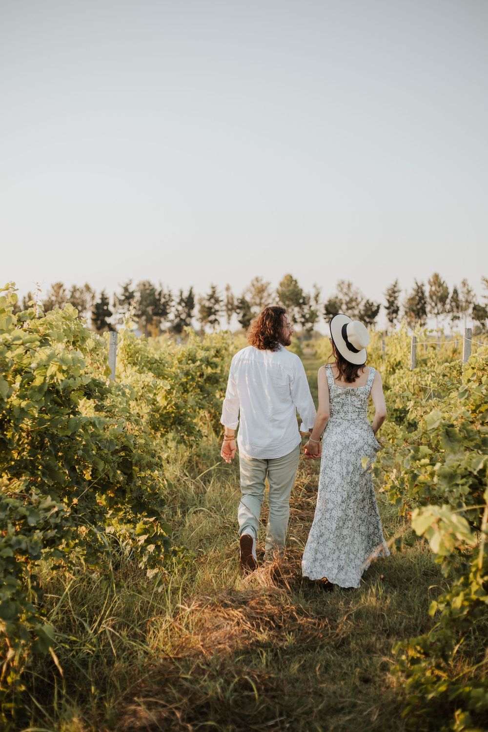 A couple strolls together through a sunlit vineyard path during golden hour.