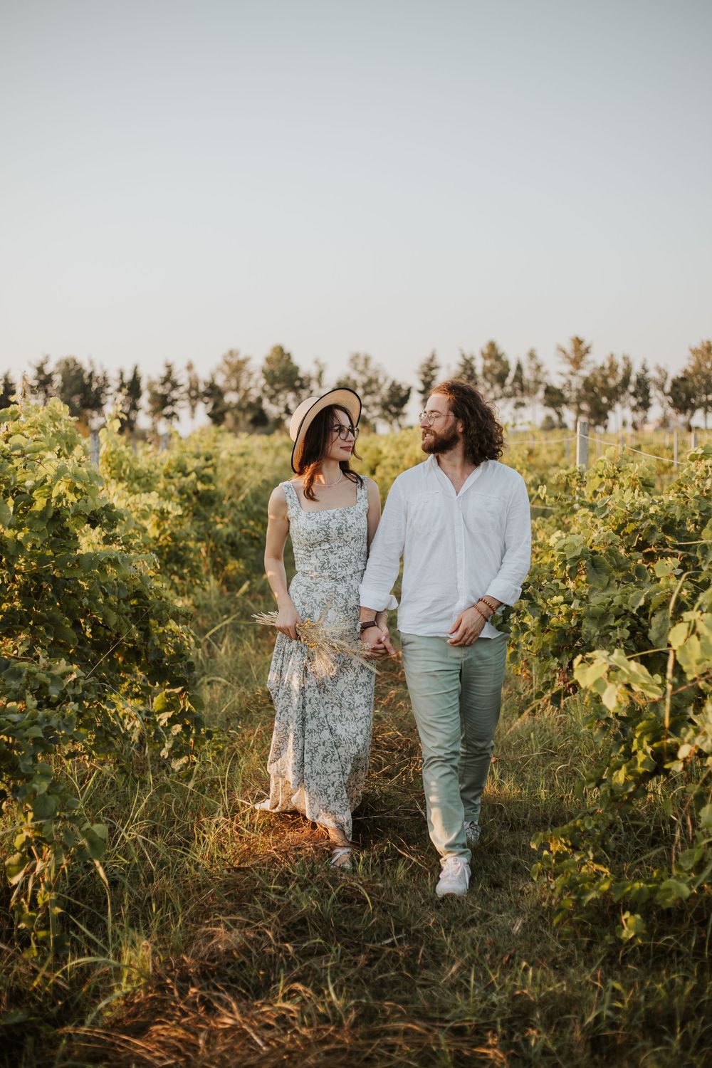 A couple in casual attire poses together among grapevines during sunset.