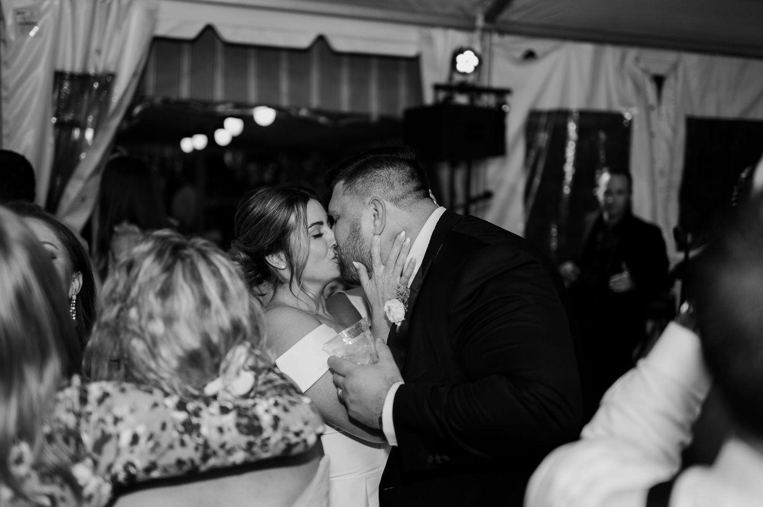 Black and white photo of guests dancing at a wedding reception under string lights.