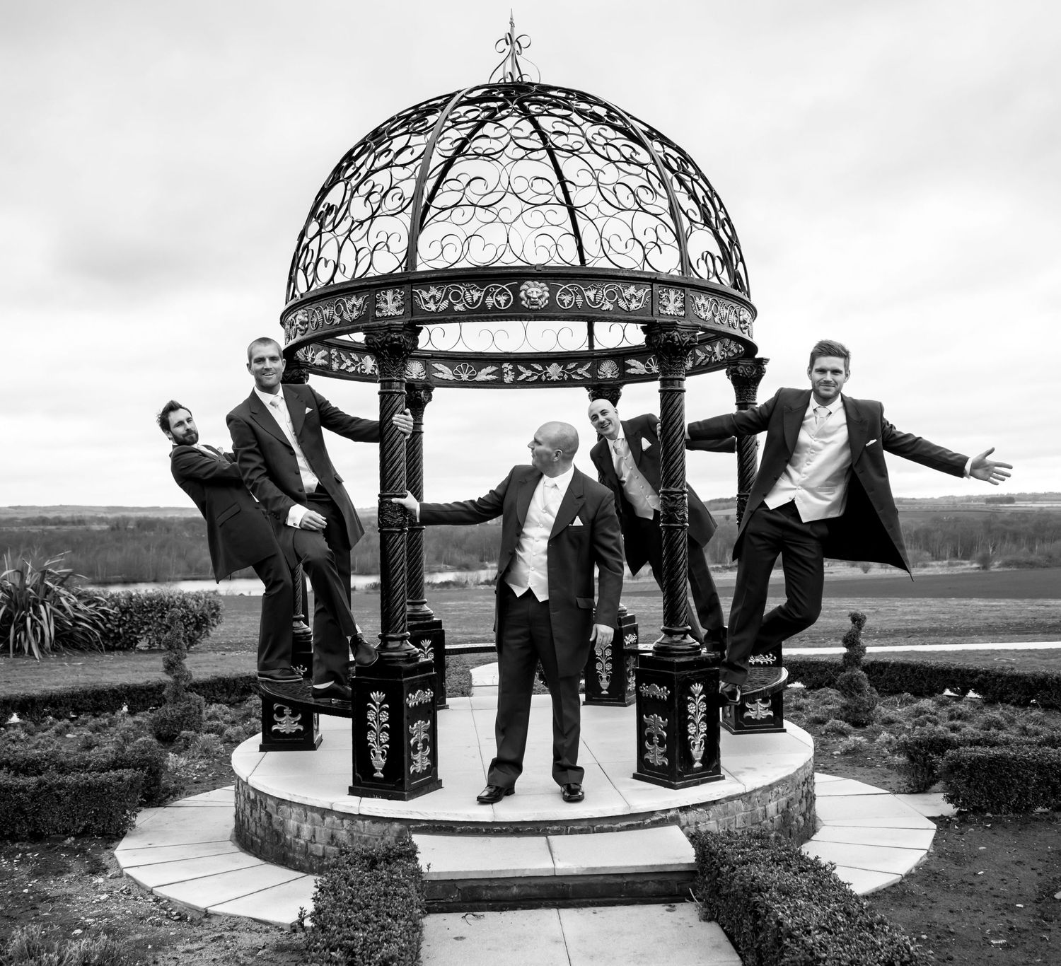 A fun group photo taken at an ornate metal gazebo in black and white.