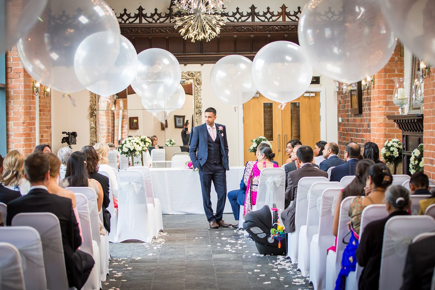 Indoor wedding ceremony venue decorated with white balloons and elegant lighting.