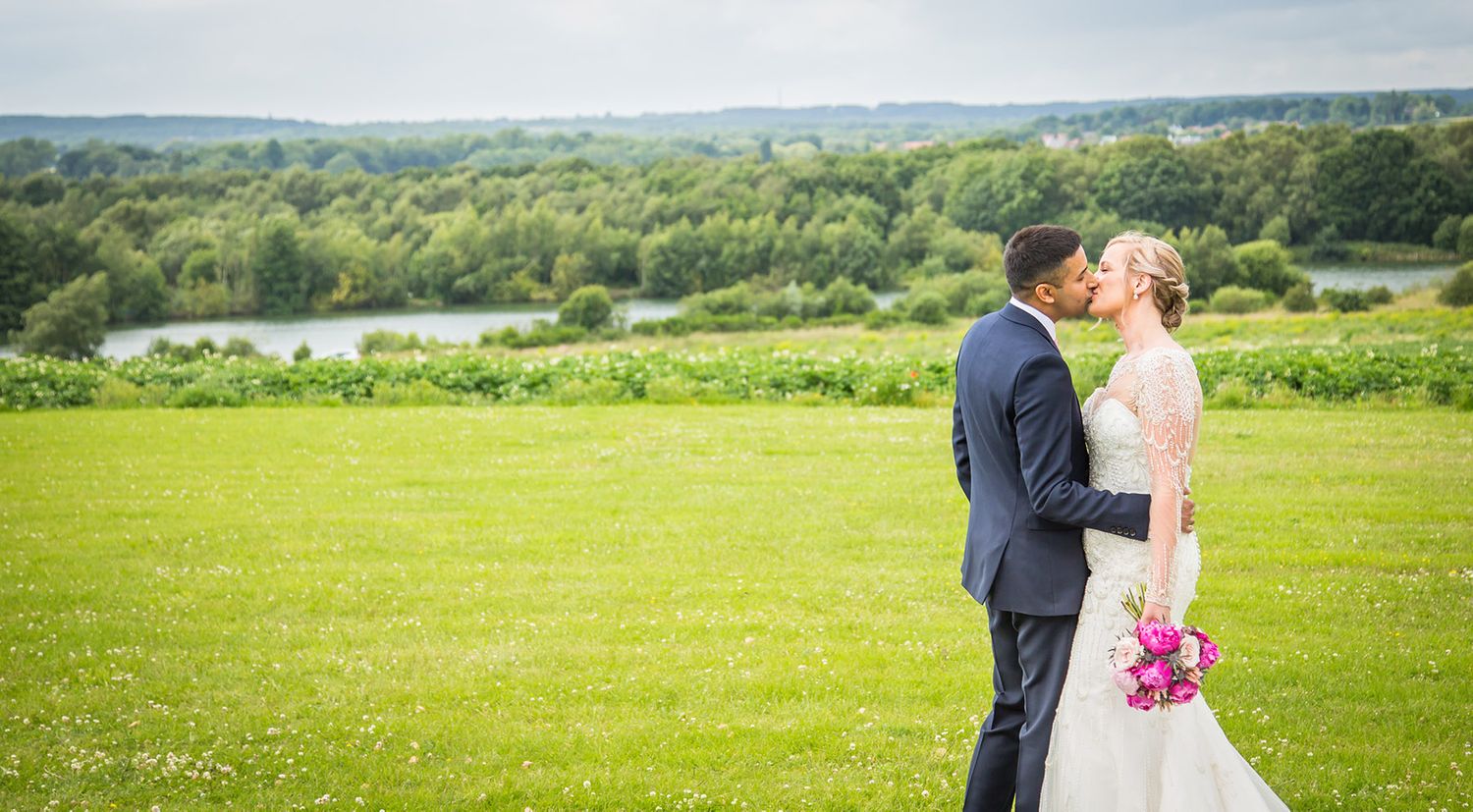 Wedding couple standing on hilltop meadow overlooking scenic lake view.