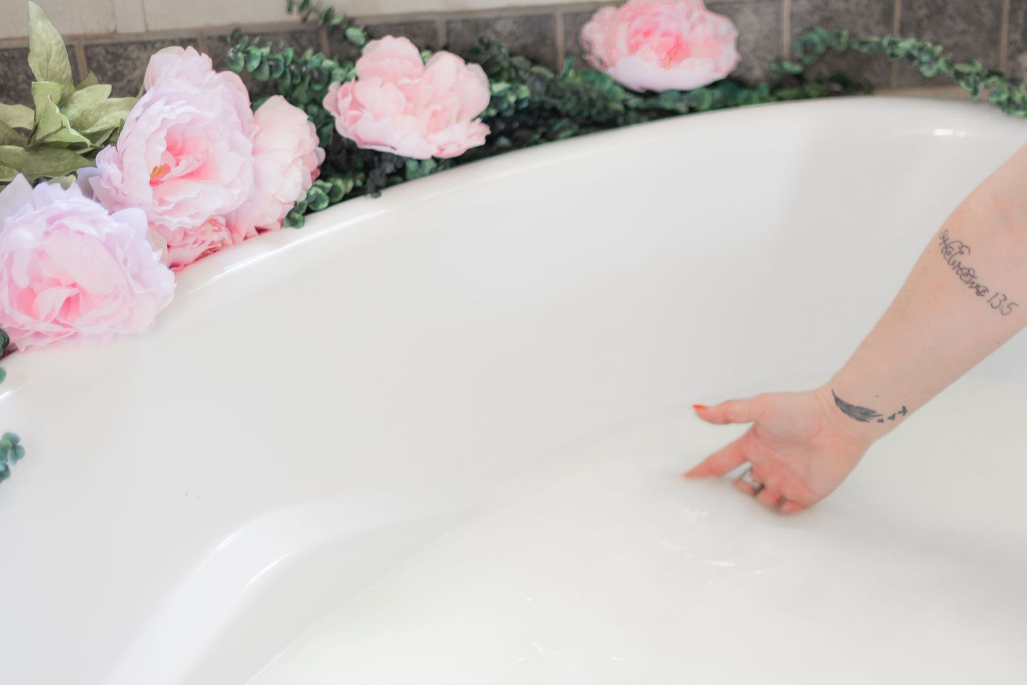 Close-up of bathtub edge decorated with pink roses and greenery.