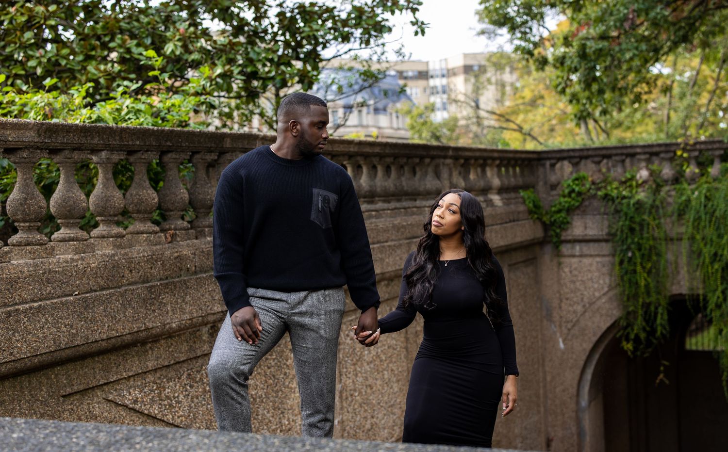 Couple in casual outfits sharing playful moment by stone balustrade outdoors.