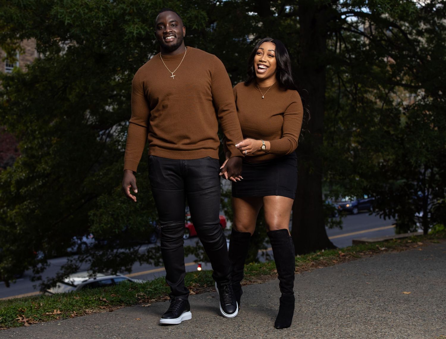 Couple in matching brown sweaters walking together on autumn path.