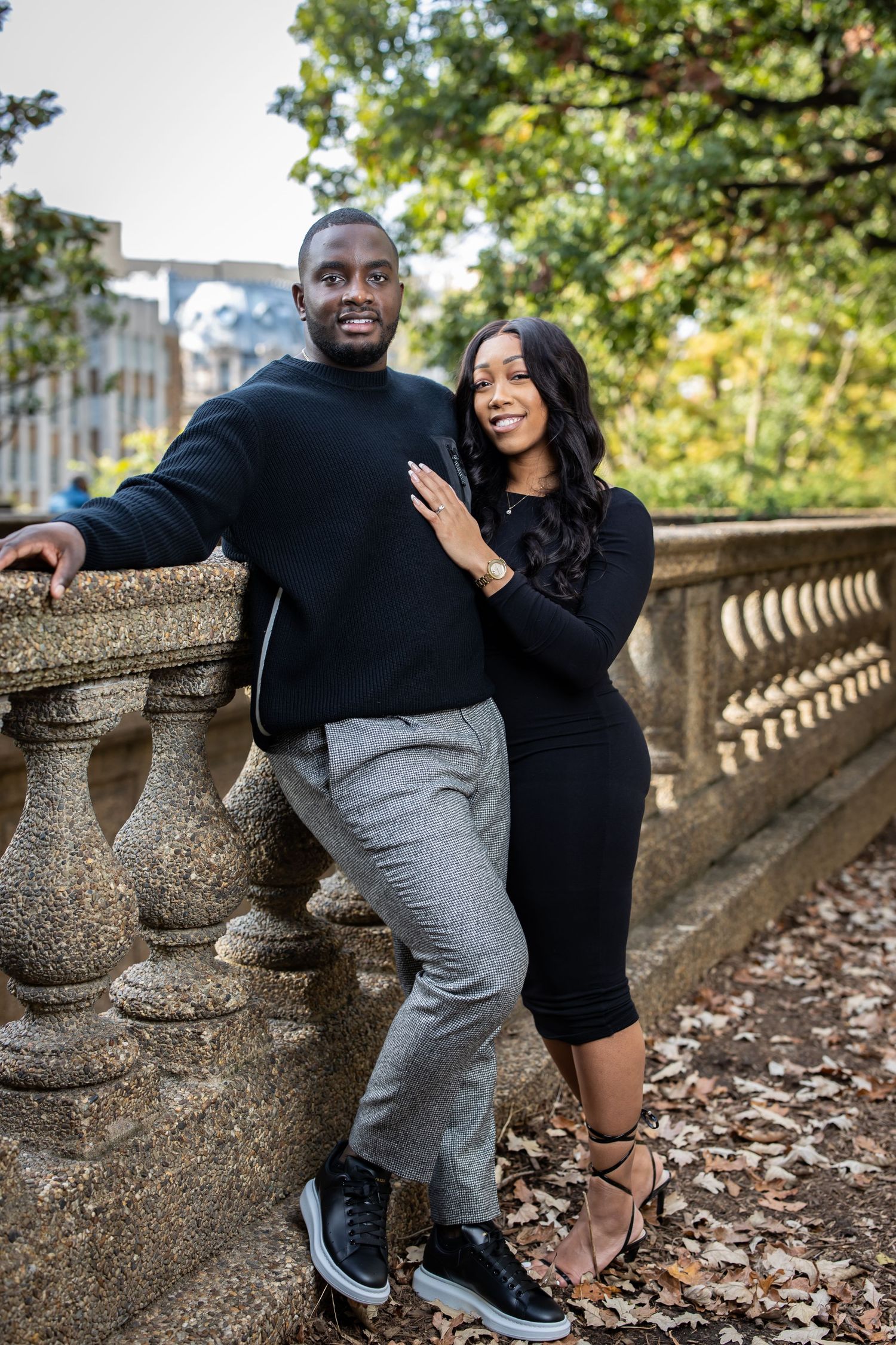 Couple sharing joyful moment while posing by ornate stone balustrade in park setting.