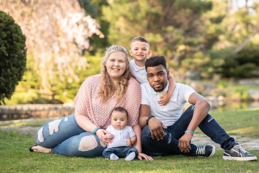 A loving family sitting together on grass in a scenic garden setting.