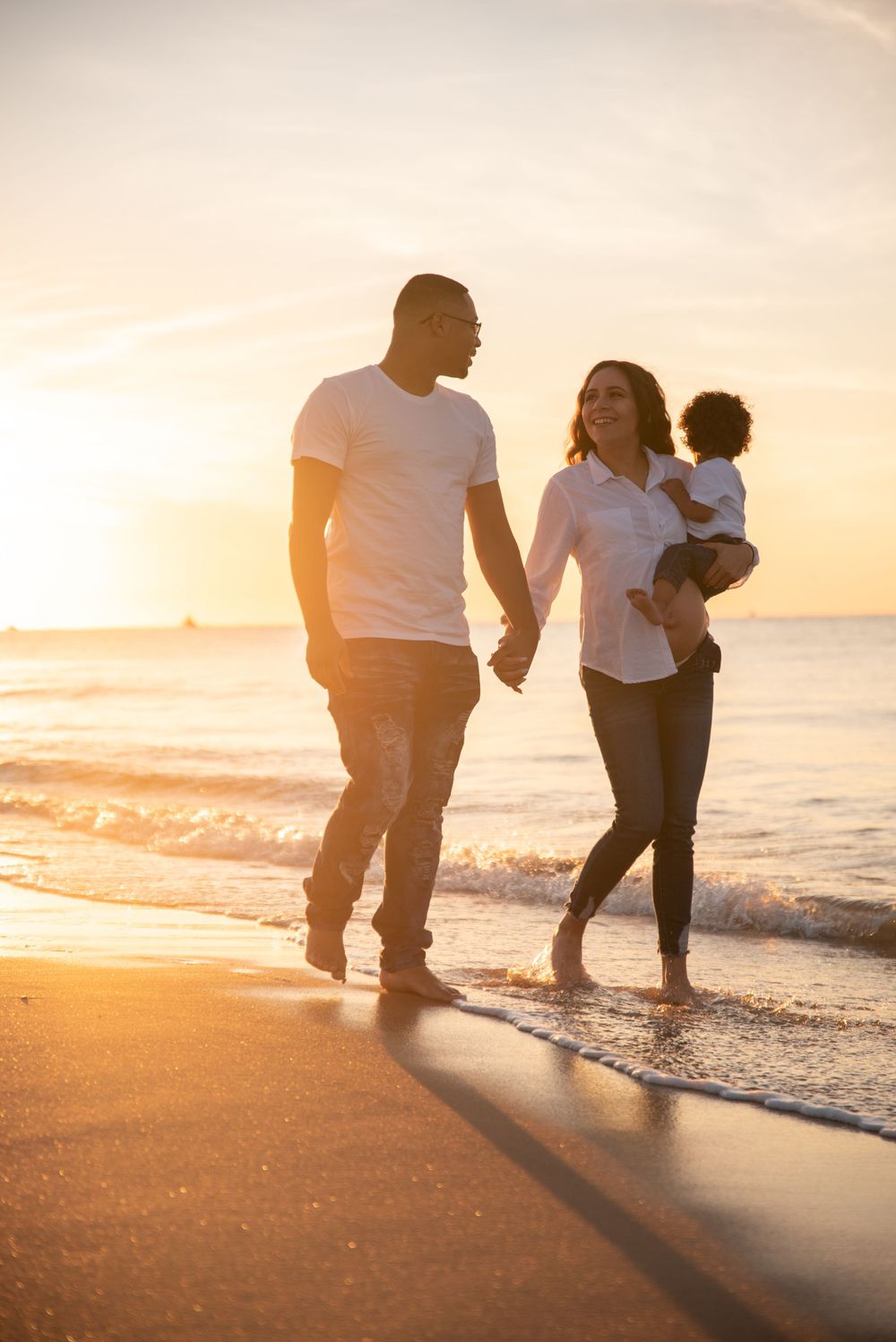 Family walking along beach at sunset holding hands with waves crashing behind them.