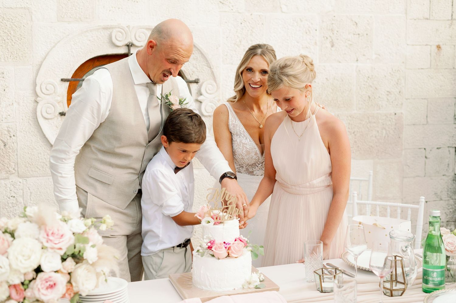 Intimate family moment at an elegant wedding cake cutting with soft pink floral decorations.