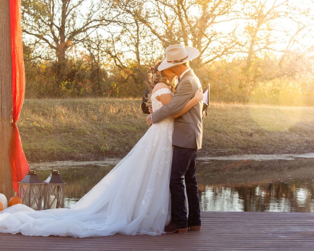 Newlywed couple embraces on wooden dock at sunset.