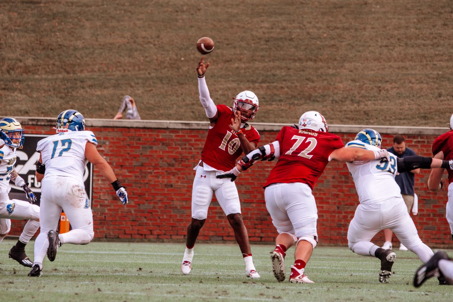 Quarterback throws football while protected by offensive line during college game.