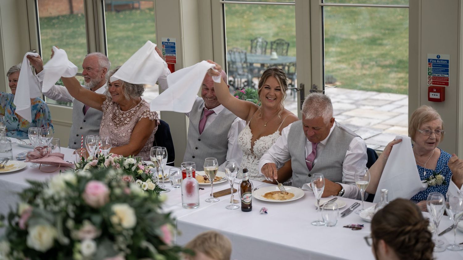 Wedding reception scene with guests waving white napkins at decorated dining tables.
