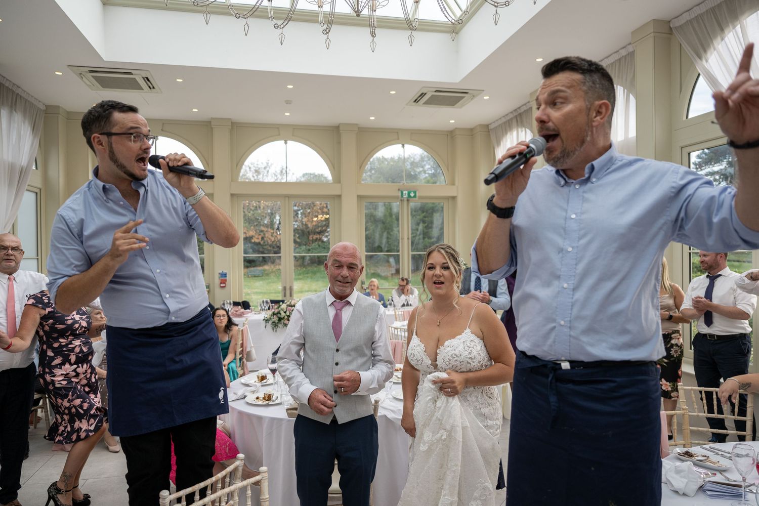 Wedding entertainment performers singing at reception in bright conservatory setting.
