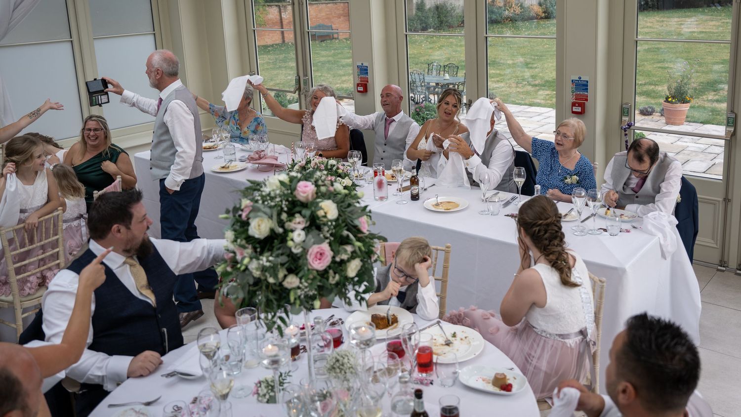 Wedding reception table decorated with floral centerpieces and formal place settings in sunlit venue.