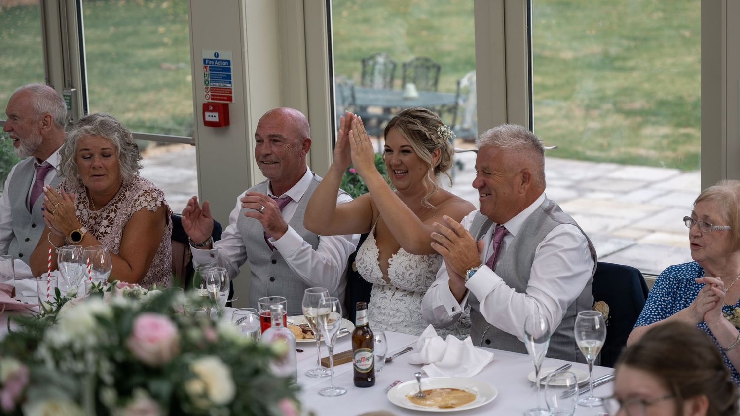 Wedding celebration with guests raising glasses during joyous toast in glass-walled reception venue.
