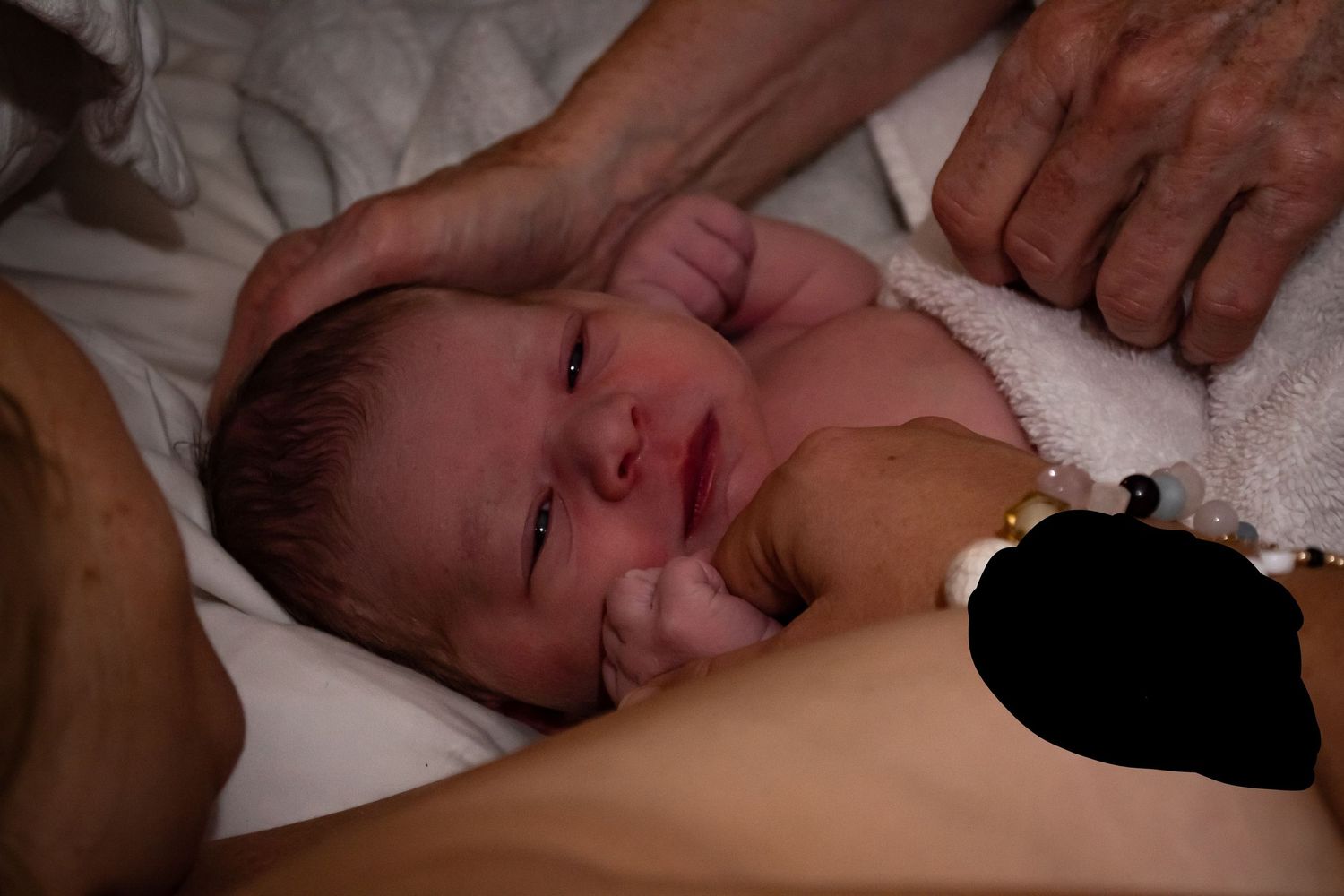 Image of a newborn baby holding her mother's hand as a midwife feels for the soft spot on her head.