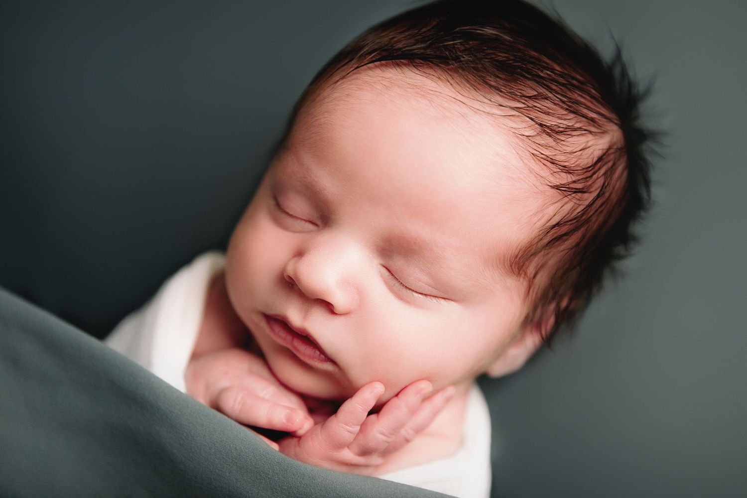 sleeping infant on teal blue background hand holding cheek