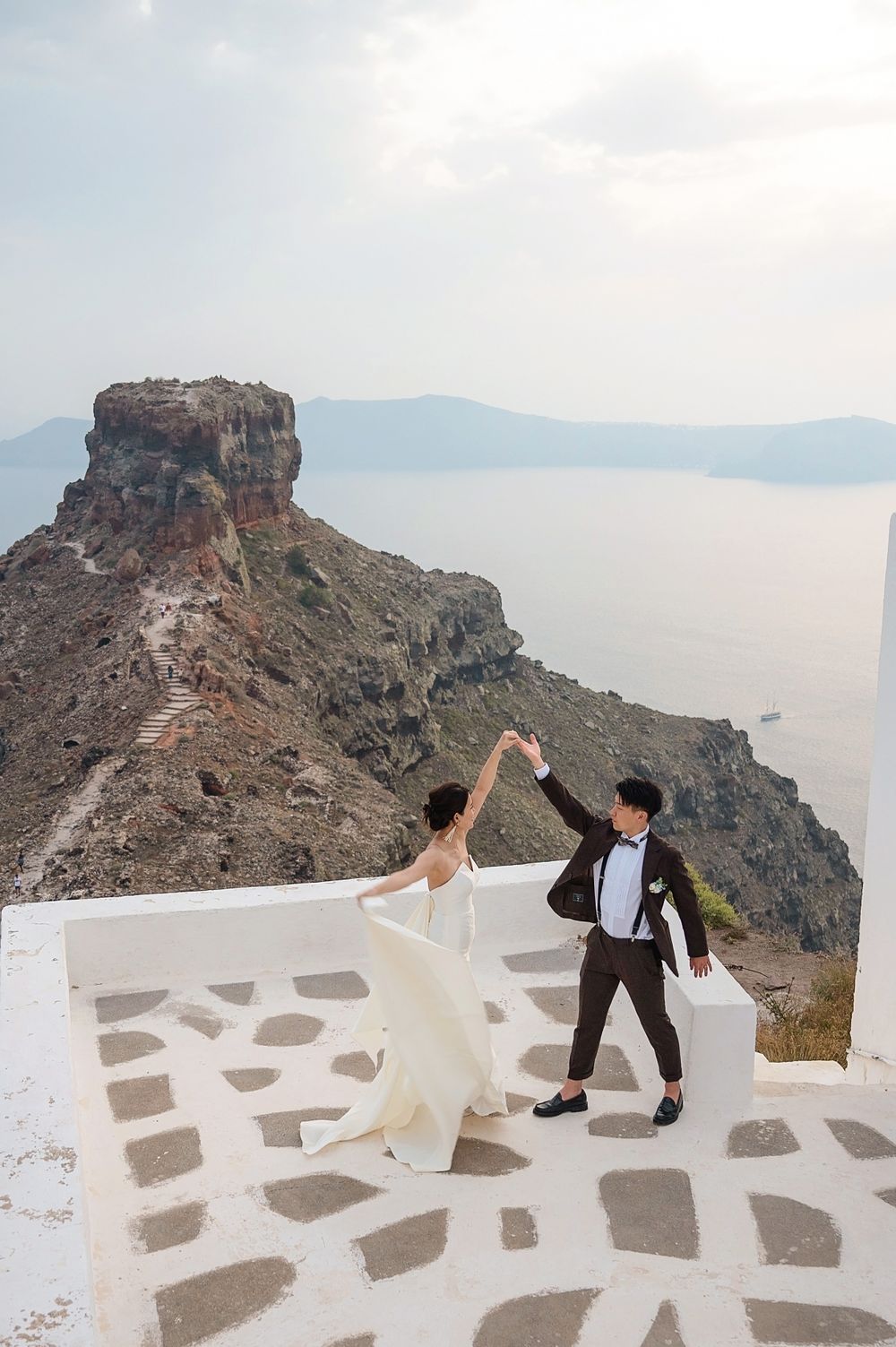 Couple dancing on white stone terrace with dramatic cliff views in Santorini.