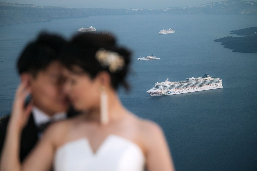 Cruise ships visible in background of intimate wedding portrait in Santorini.