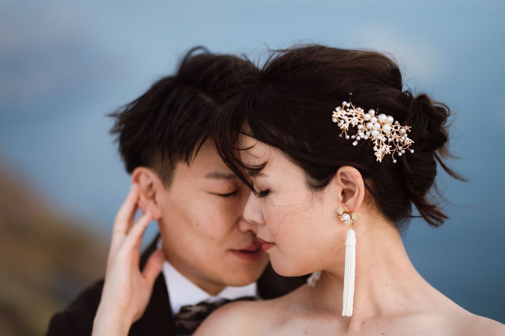 Romantic close-up of newlyweds with bride wearing floral hair accessory and white tassel earrings.