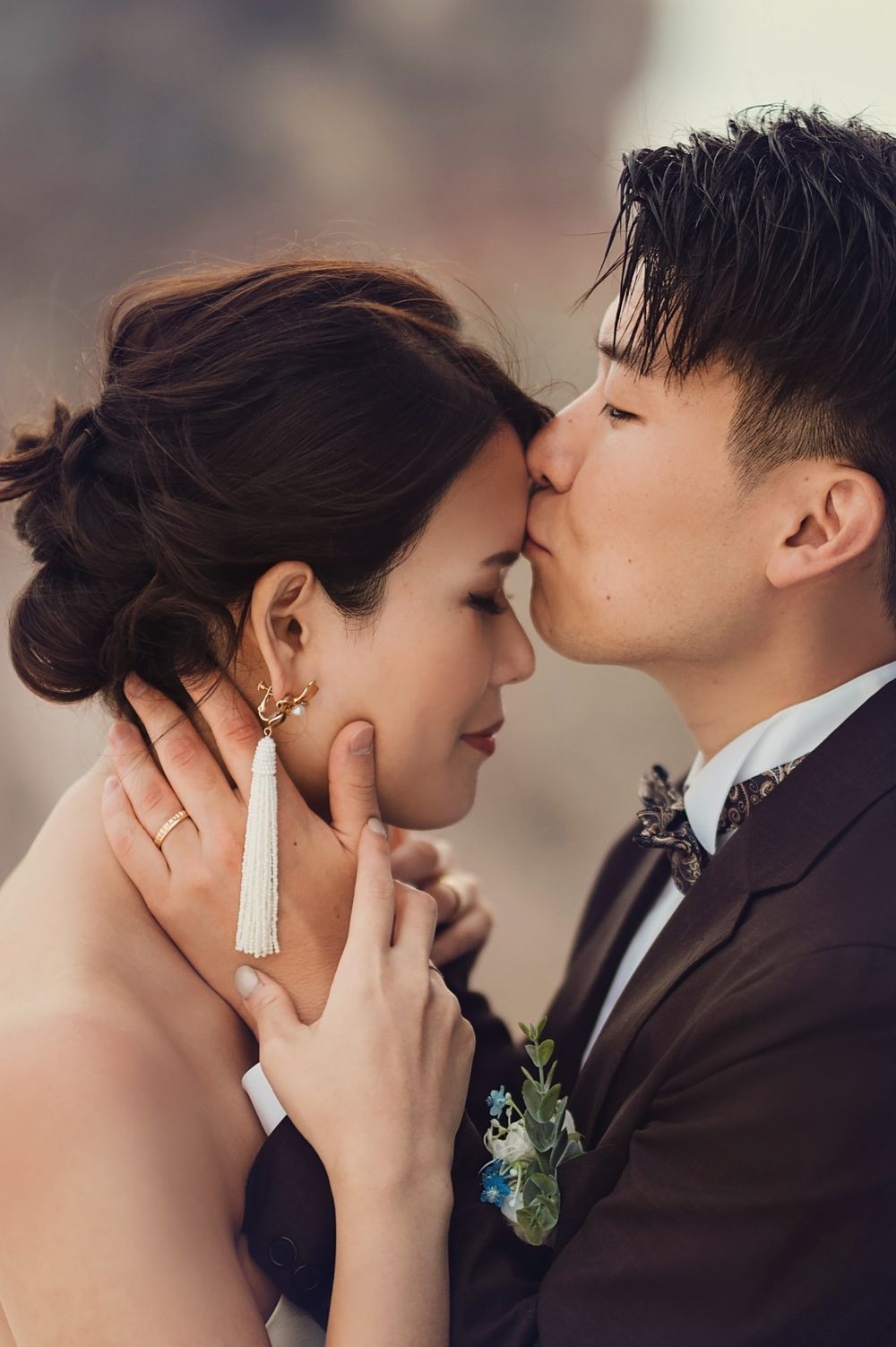 Close-up wedding portrait of couple sharing tender moment with bride wearing elegant tassel earrings.
