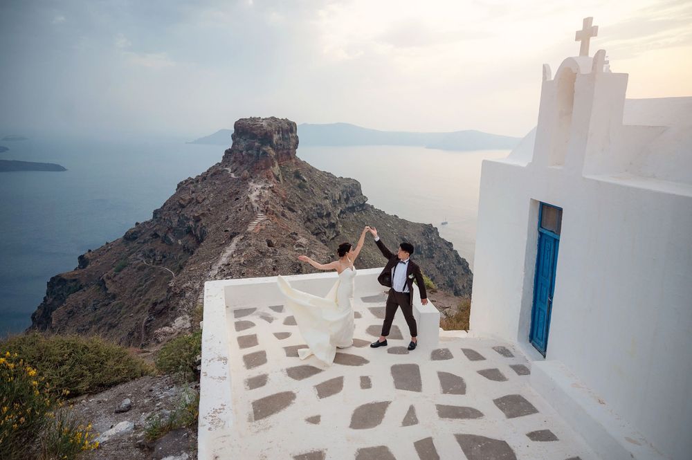 Wedding couple celebrates on church steps with scenic Aegean Sea views.