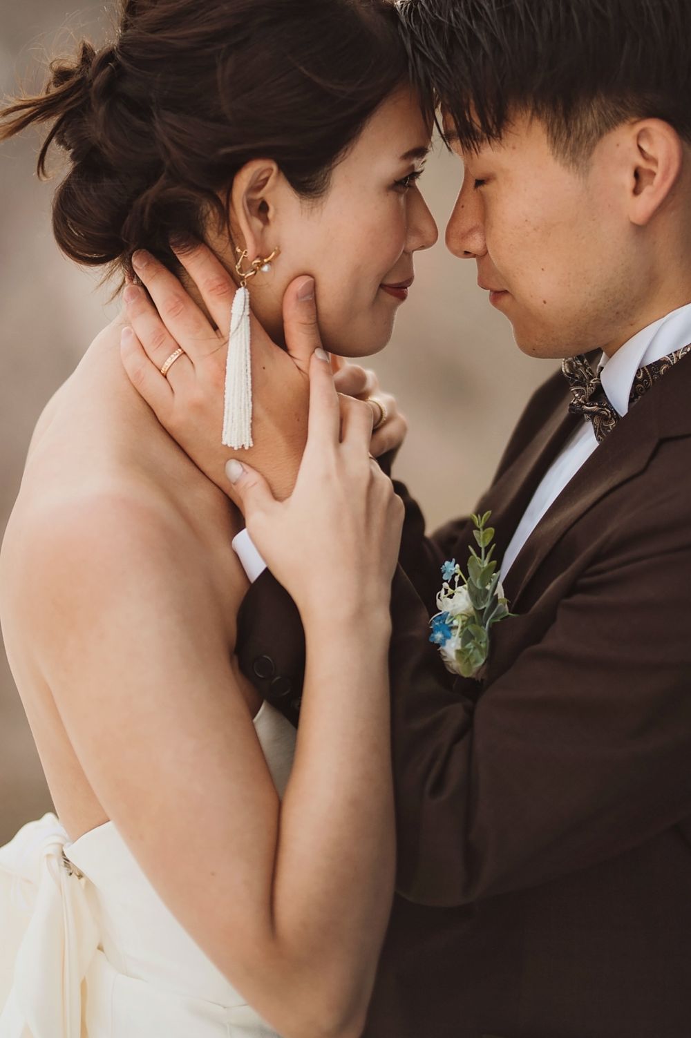 Romantic close-up of newlyweds in intimate pose with bride wearing white tassel earrings.