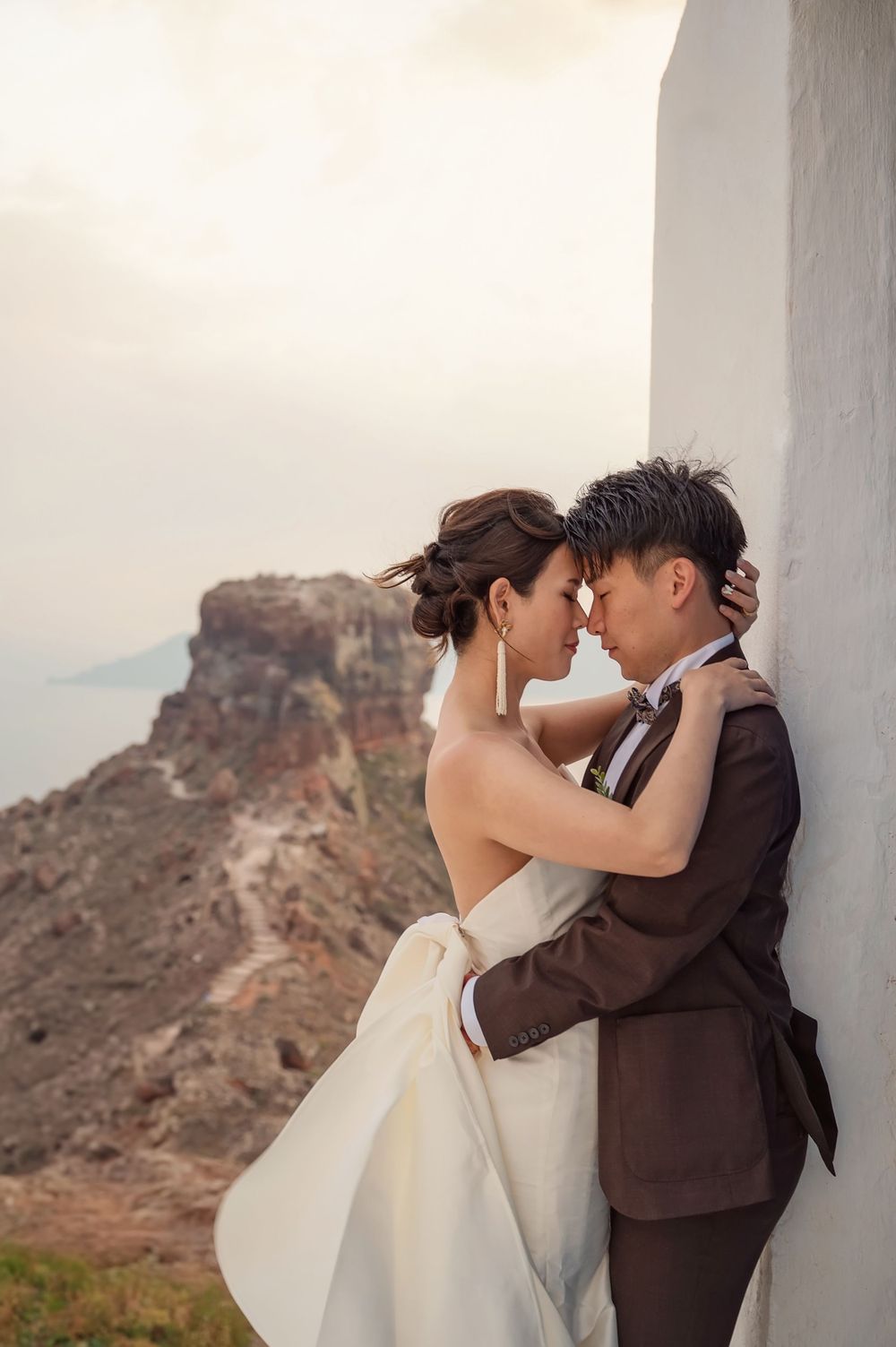 Romantic moment between newlyweds against white Mediterranean architecture with cliffside views.
