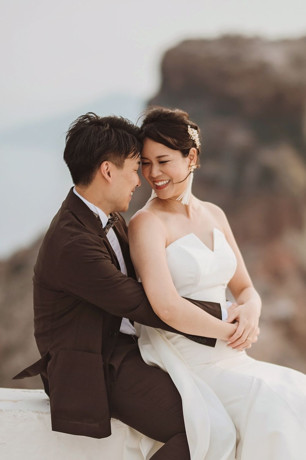 Candid wedding portrait of couple sitting together on white surface with mountain backdrop.