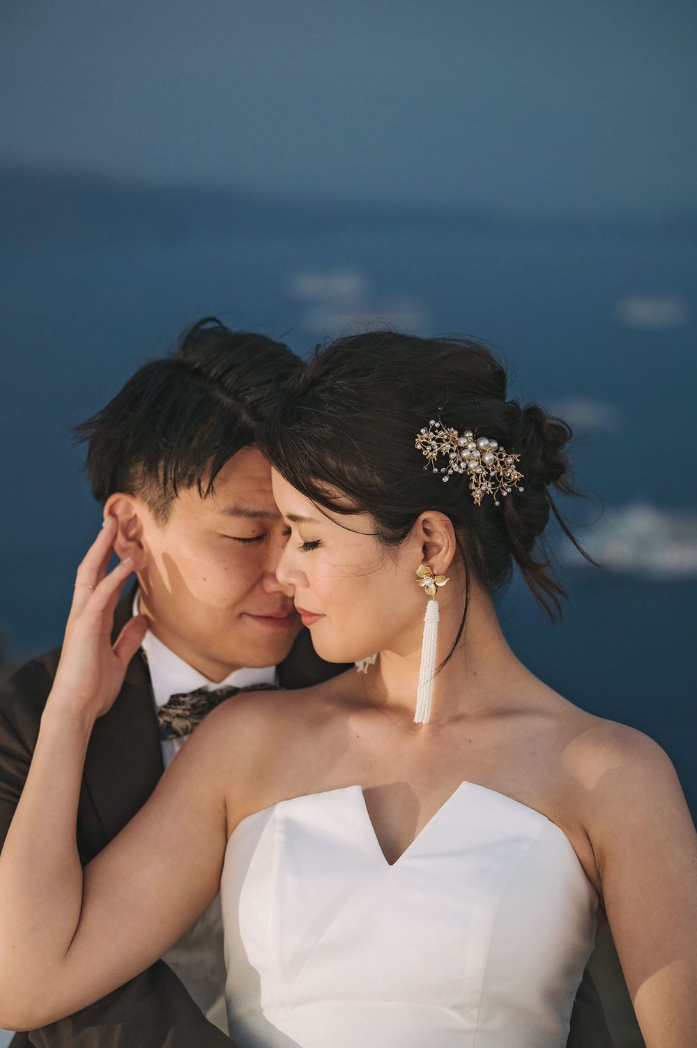 Close-up wedding portrait with bride wearing crystal hair accessory against ocean backdrop.