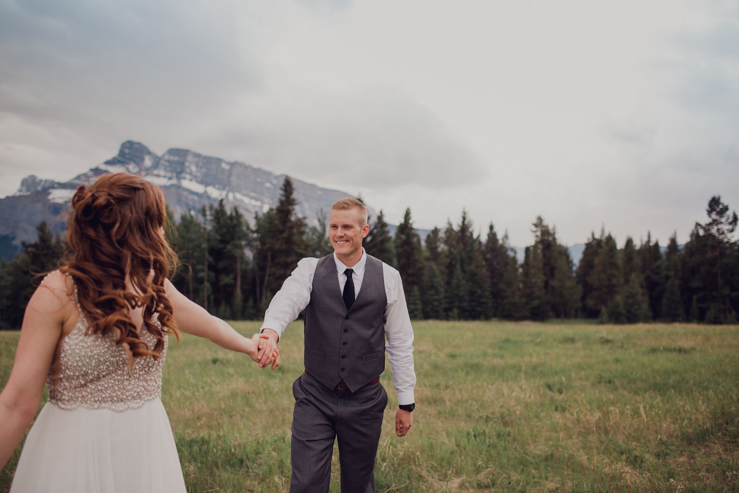 A couple hand in hand on their wedding day  walks through mountain meadows in Banff Alberta