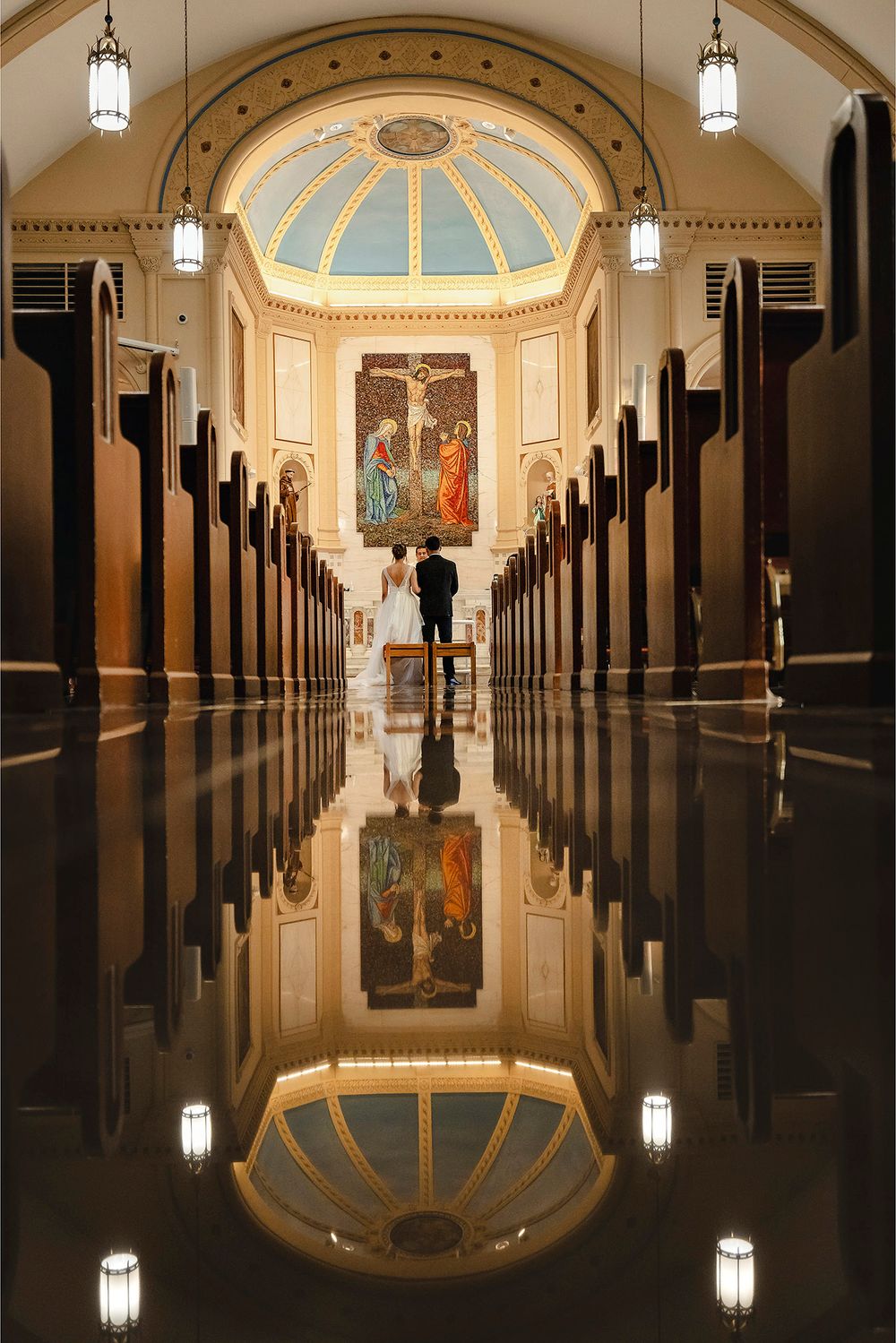 Elegant church interior with symmetrical pews and ornate domed ceiling reflecting on polished floor.