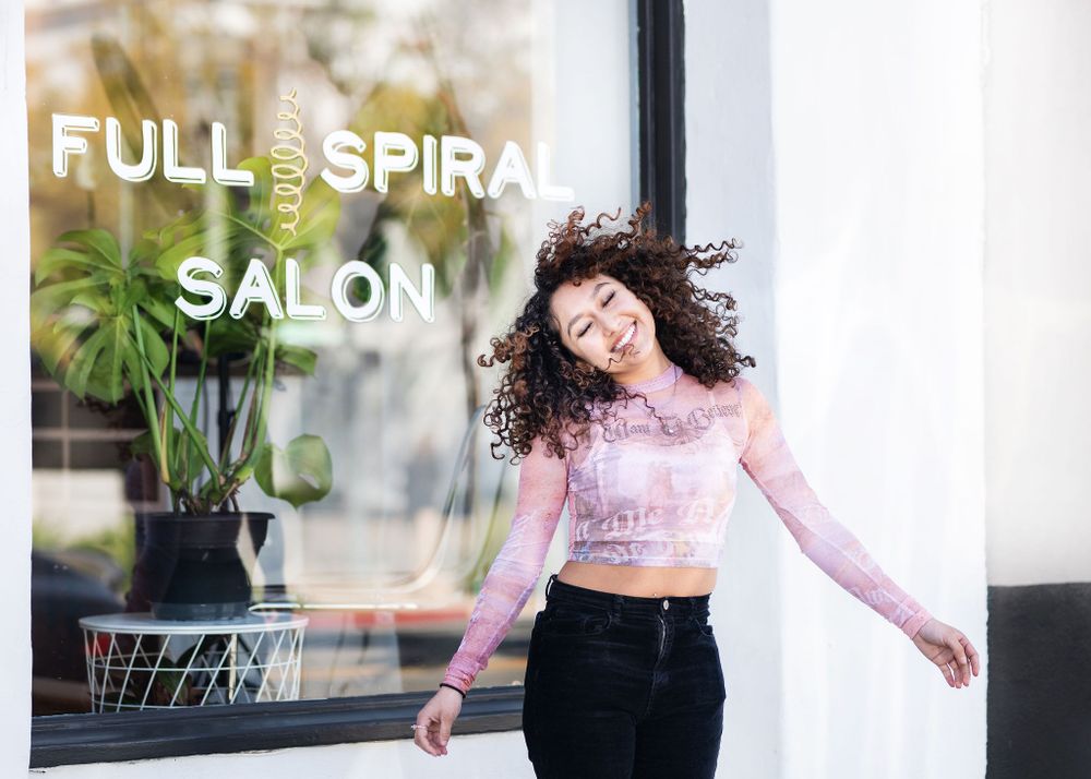 woman with curly hair laughing outside of full spiral salon after haircut