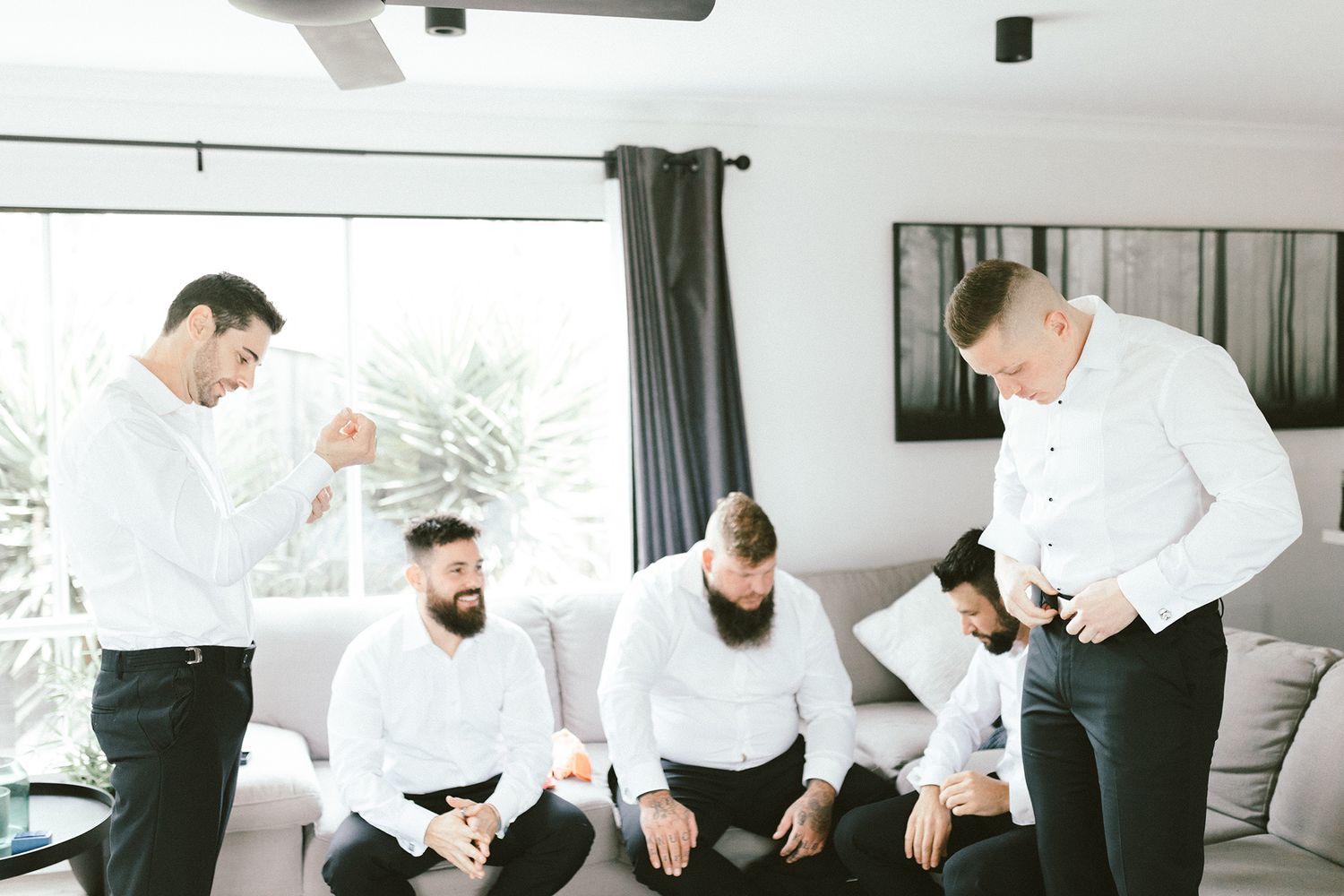 A group of men in white shirts gather in a modern living room for formal preparations.