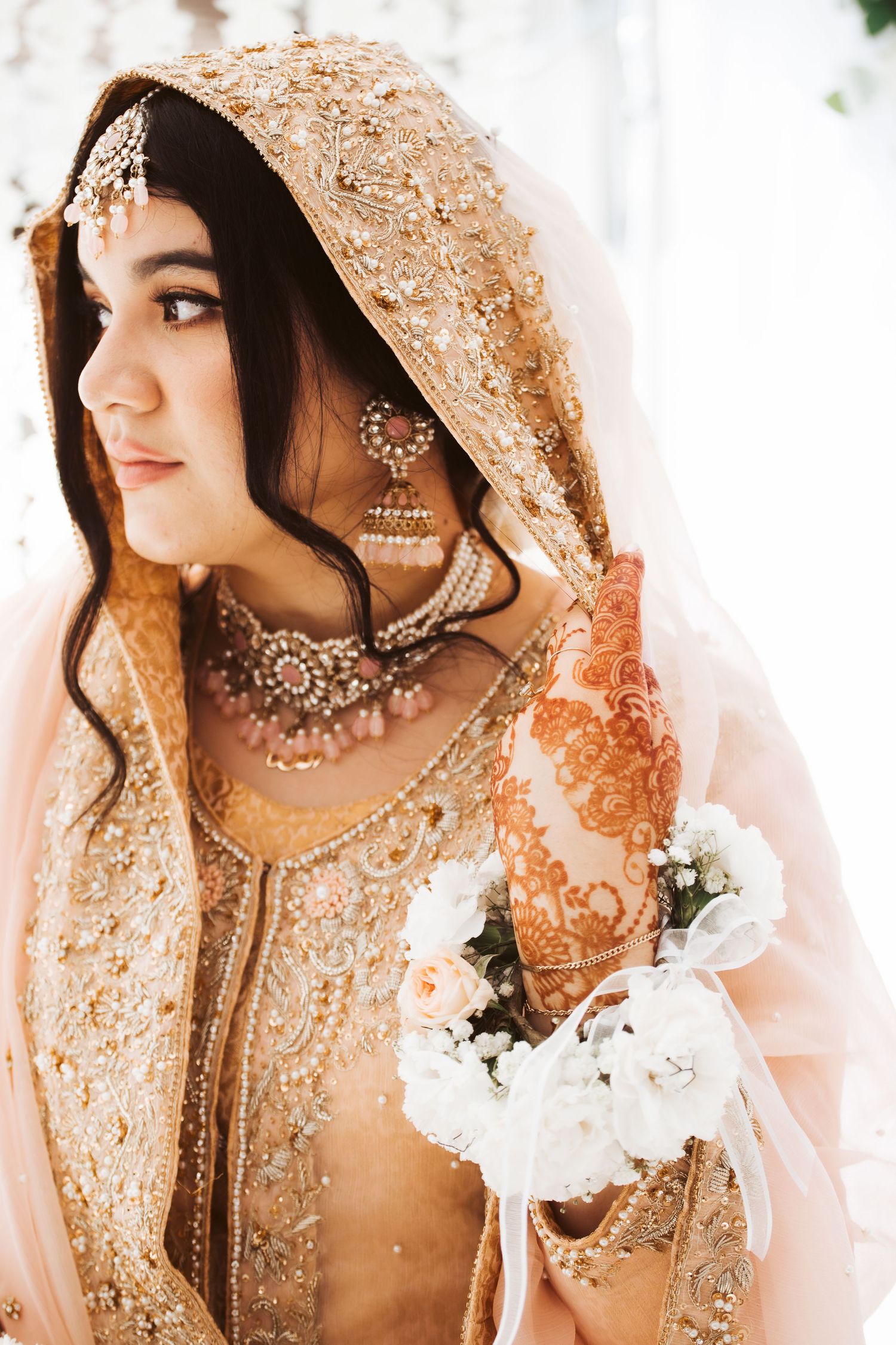 A traditional South Asian bride wears an intricately beaded gold outfit with matching jewelry.
