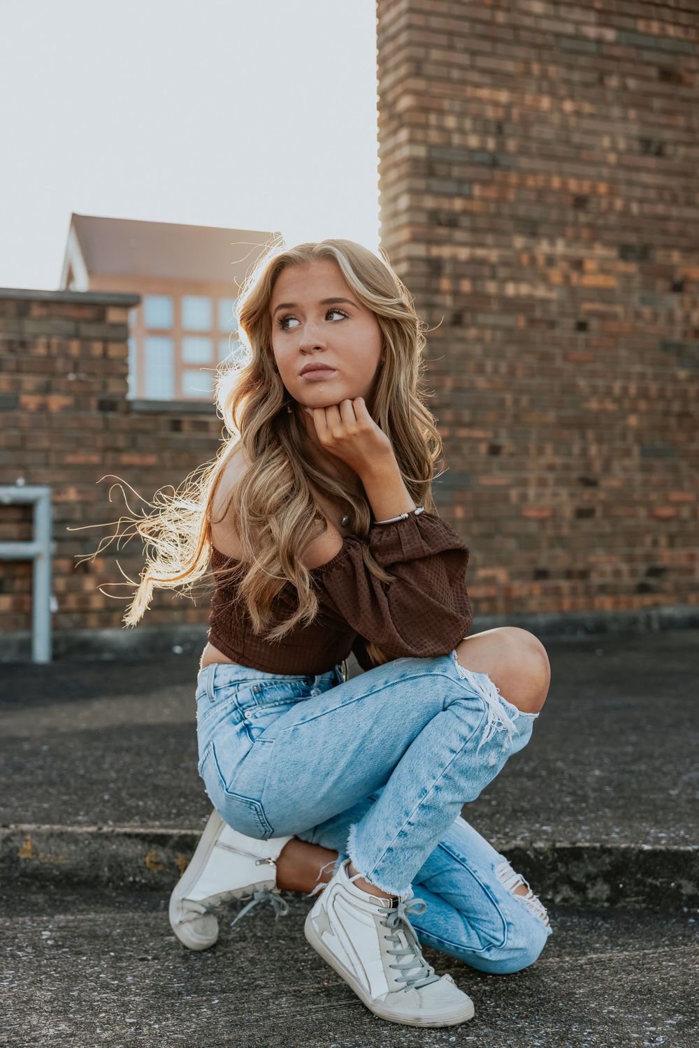 Casual fashion portrait featuring light denim jeans and white sneakers against a brick wall backdrop.